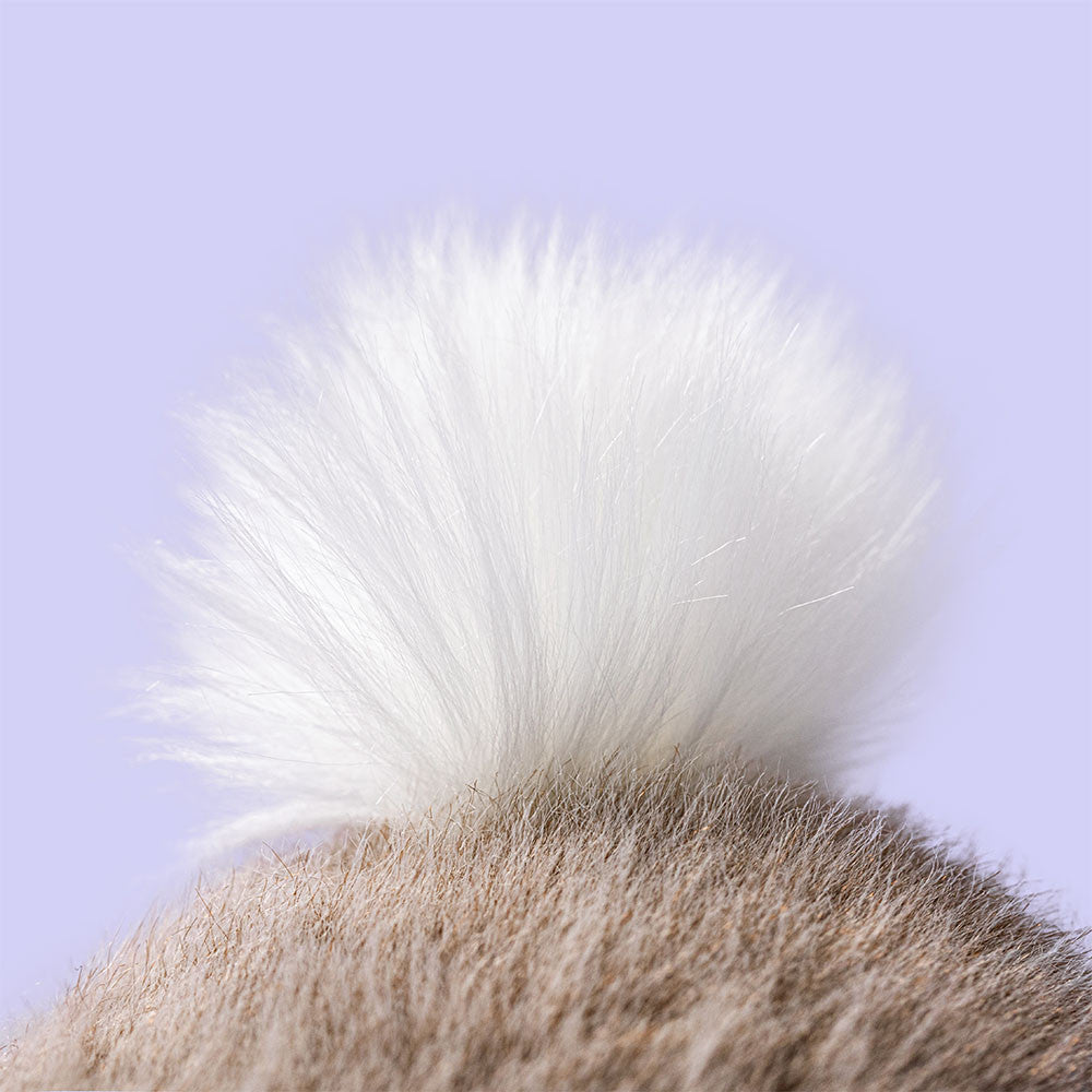 Close-up of a fluffy white cat tail against a light purple background