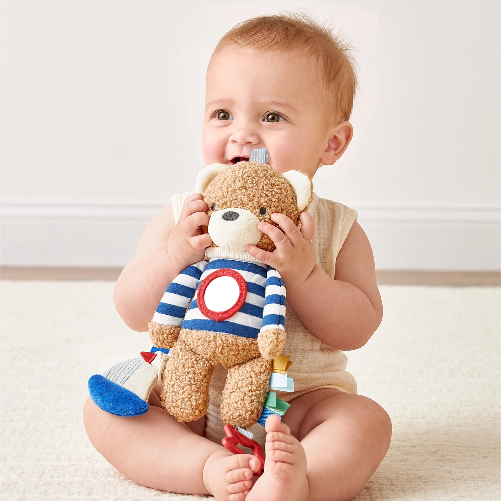 Baby holding a teddy bear with a striped sweater on a light background