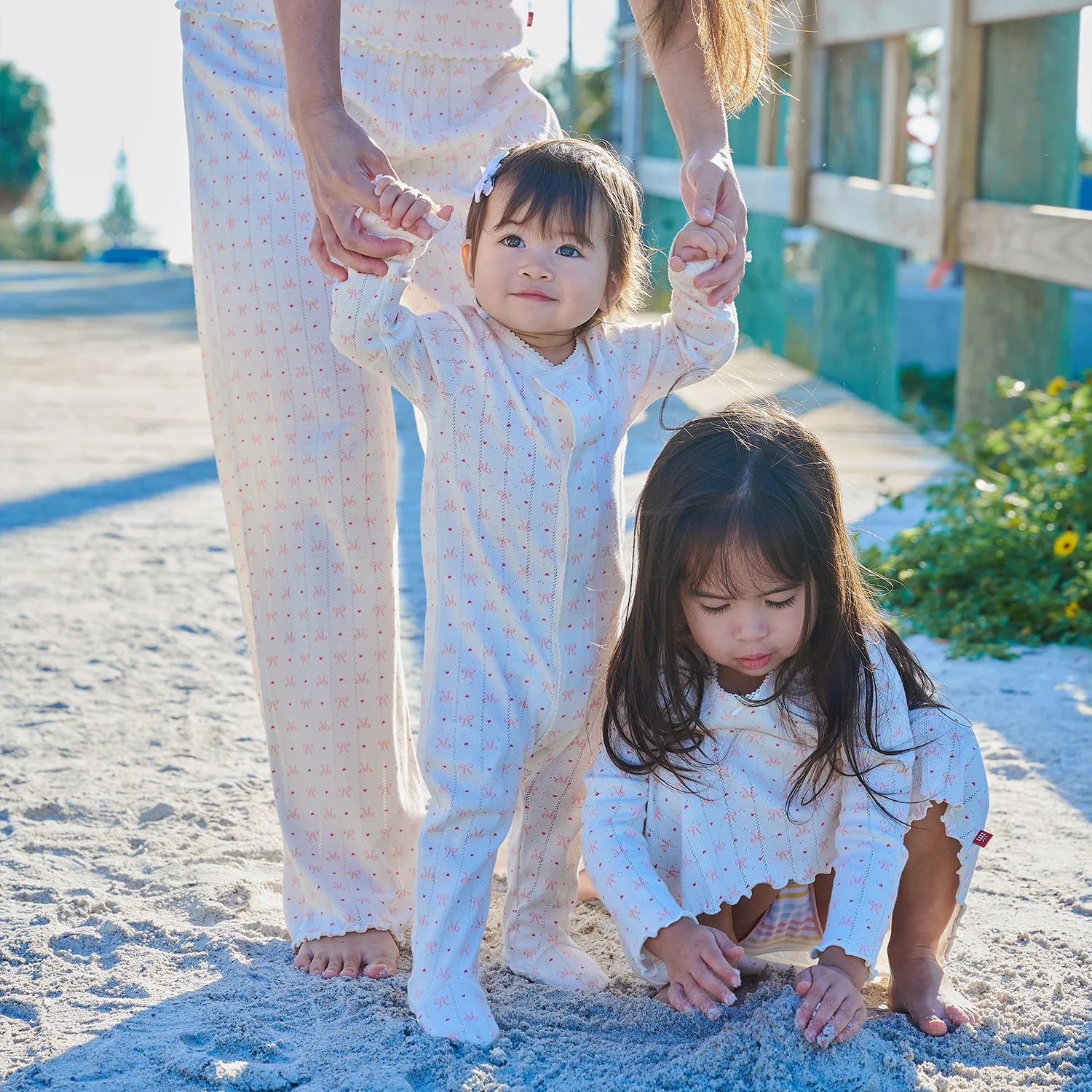 Two young girls in matching outfits standing on a sandy beach with an adult.