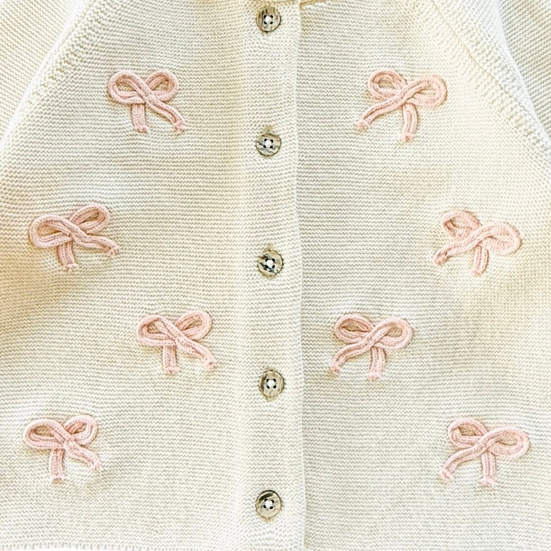 Close-up of a warm white-colored cardigan with pink bows and wood buttons.