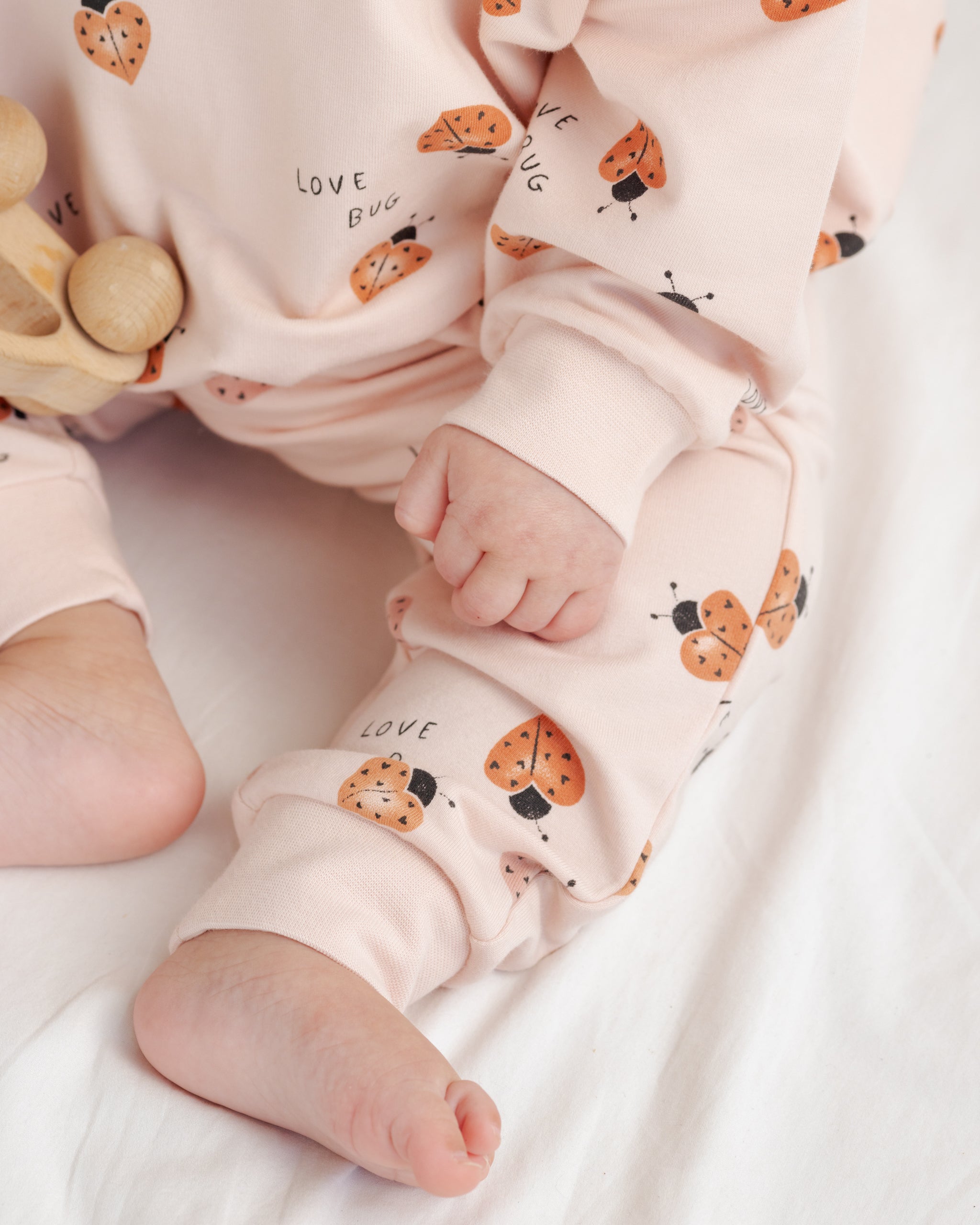 Baby wearing pink pajamas with ladybug pattern on a white blanket