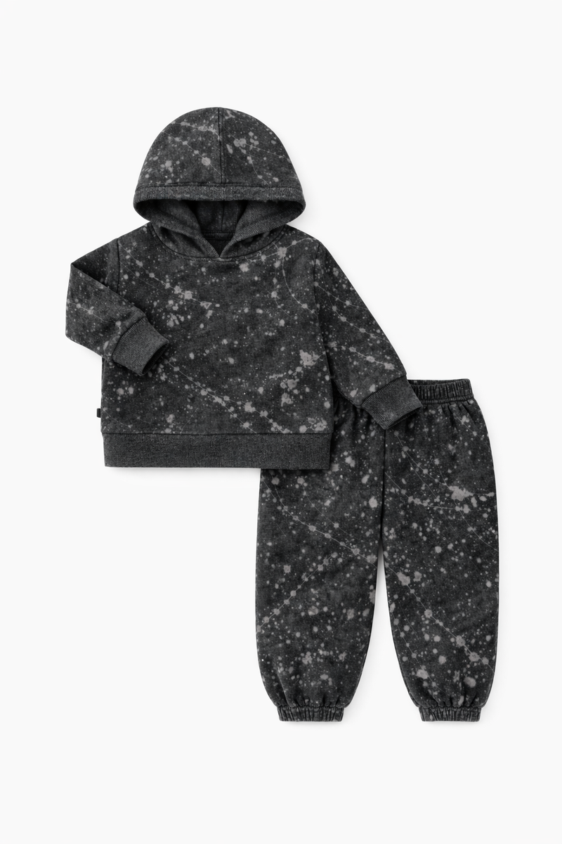 A two-piece children's loungewear set consisting of a cropped hooded sweatshirt and matching jogger pants, both in a washed black fabric with a white speckled or splatter-like print, shown on a plain white background.