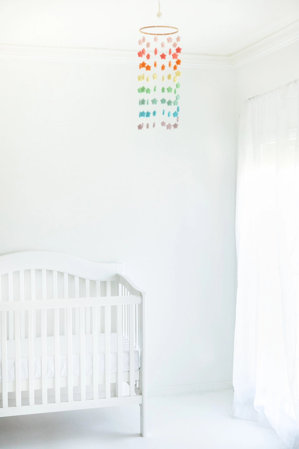 White crib in a room with a colorful hanging mobile against a white wall.