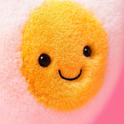 Yellow plush toy with a smiley face on a pink background