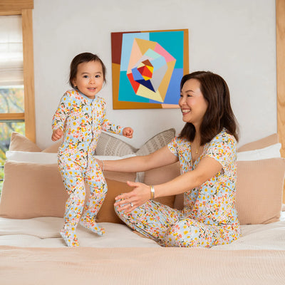 Woman and child in matching floral pajamas on a bed with a colorful abstract painting in the background.