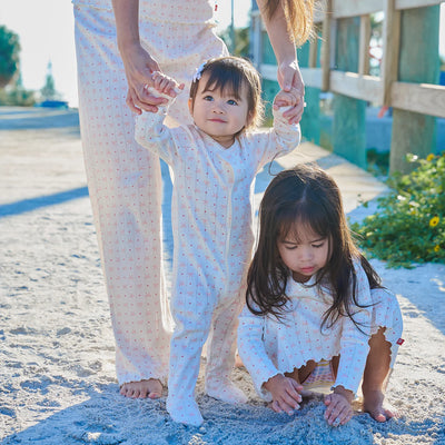 Two young girls in matching outfits standing on a sandy beach with an adult.