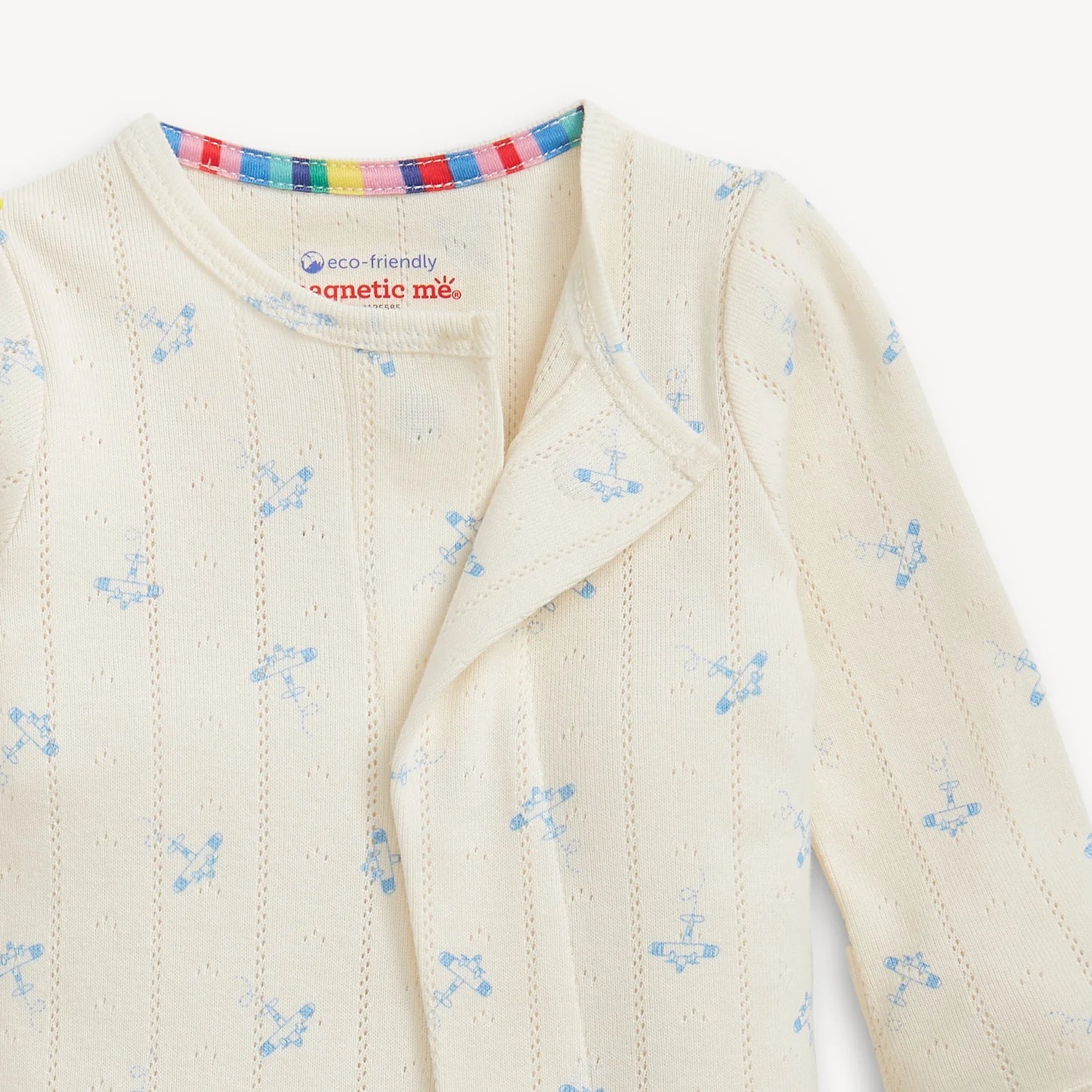 Close-up of a cream-colored baby outfit with airplane pattern and  cream colored trim on a white background.