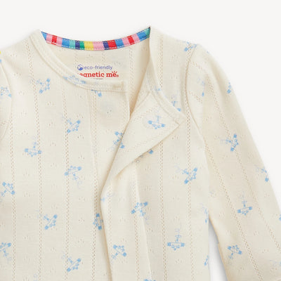 Close-up of a cream-colored baby outfit with airplane pattern and  cream colored trim on a white background.