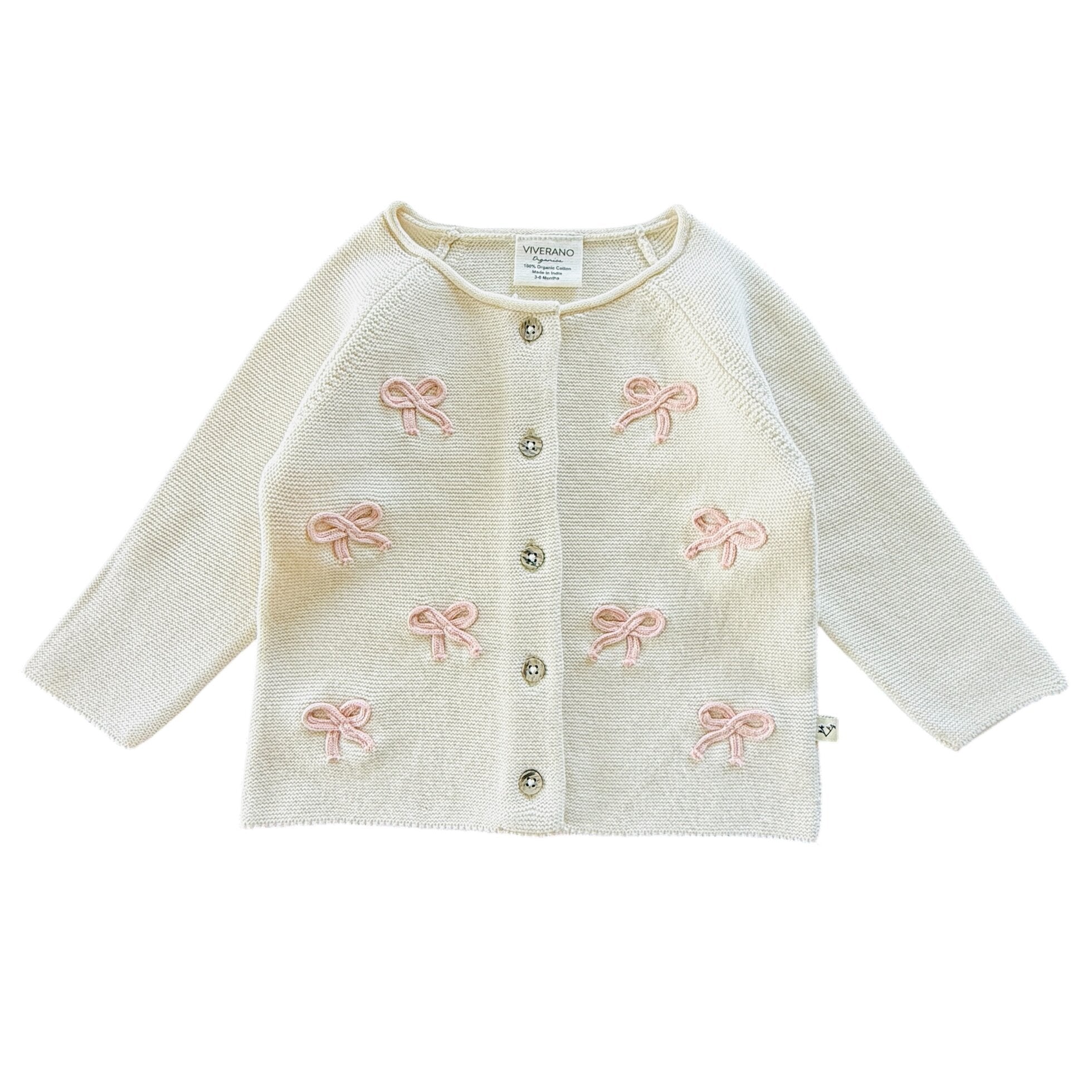 Warm white baby cardigan with pink bow details on a white background