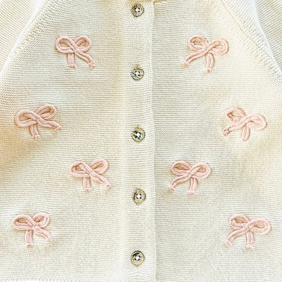 Close-up of a warm white-colored cardigan with pink bows and wood buttons.