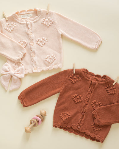 Two children's sweaters, one pink and one brown, with floral patterns on a light background.