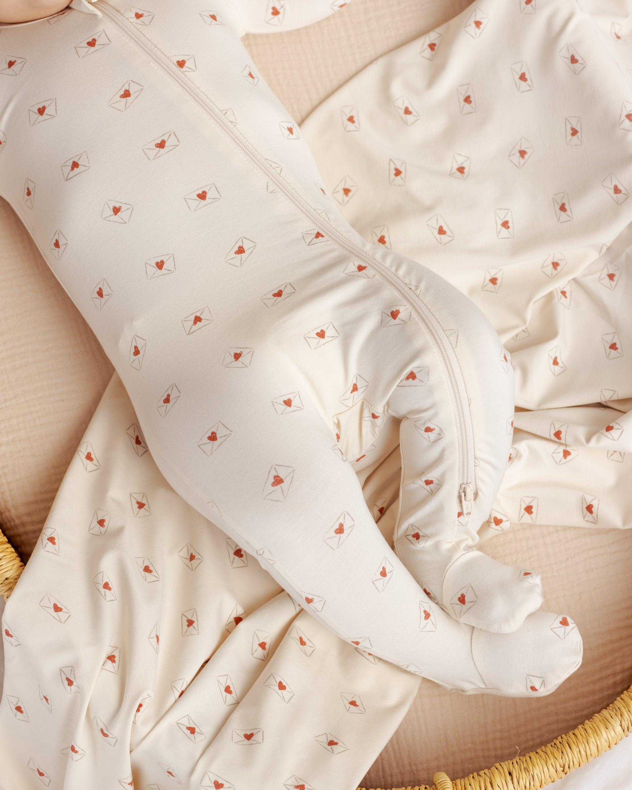 Close-up of a baby in a white outfit with red heart patterns, lying on a textured surface.