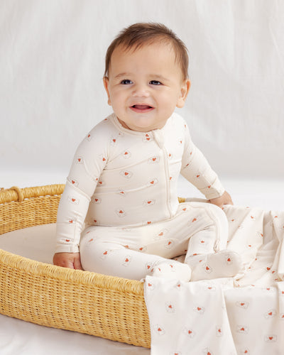 Baby in a white outfit with red patterns sitting in a wicker basket on a white background
