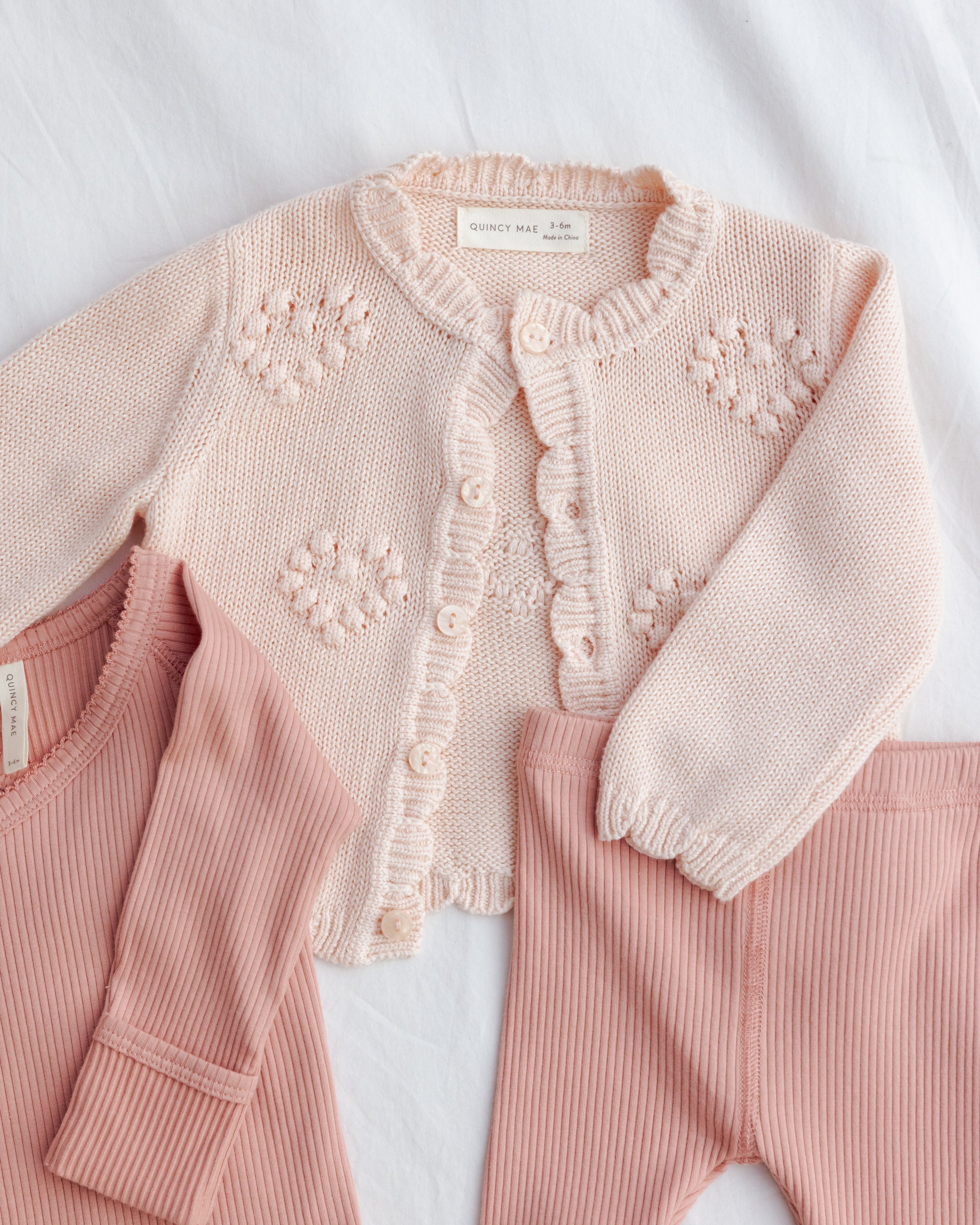 Pink baby outfit with a knitted cardigan on a white background