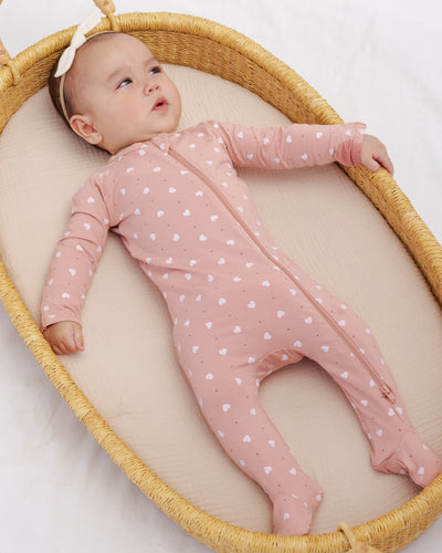 Baby in a pink polka dot onesie lying in a wicker crib with a white background