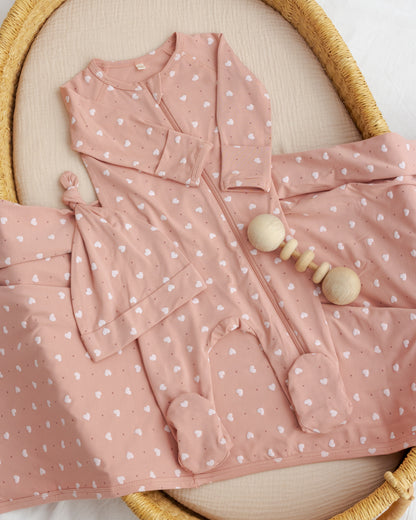Pink baby outfit with white polka dots and wooden rattle on a beige surface