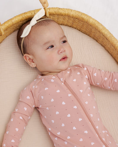 Baby in a pink heart-patterned onesie lying in a wicker basket with a white background