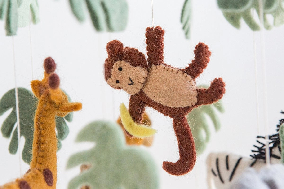 Felt monkey toy hanging among other animal toys with a leafy green background