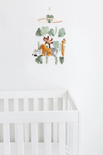 Children's crib with a jungle-themed mobile featuring animals and leaves on a white wall.