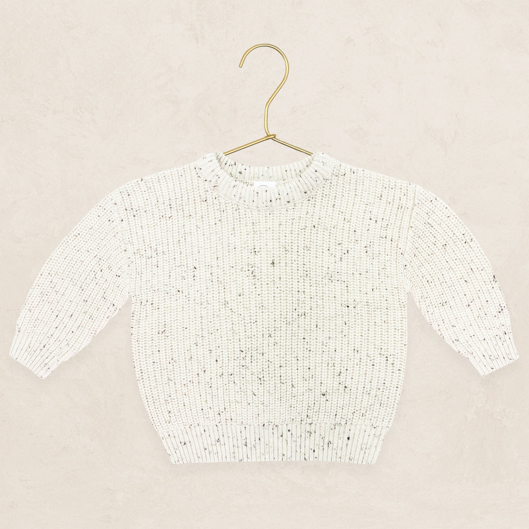 Cream speckle knit chunky sweater hanging on a gold metal hanger.