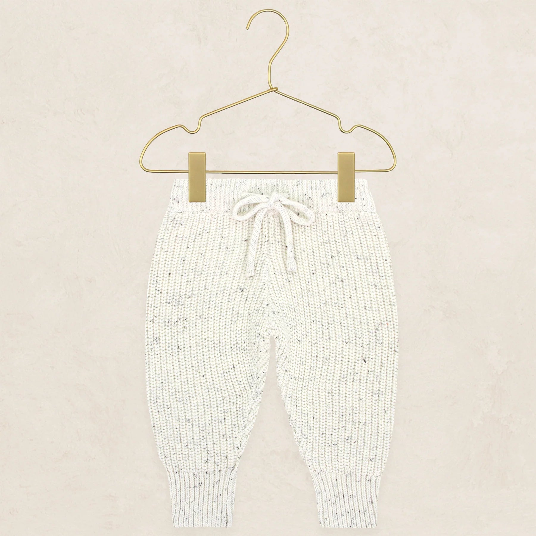 Cream speckle knit chunky jogger pants with drawstring, hung on a gold hanger.